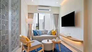 Een moderne hotelkamer met een bank, een stoel, een klein rond tafeltje, een flatscreen televisie aan de muur en een decoratief wandpaneel.