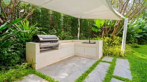 Een moderne buitenkeuken met een ingebouwde grill, omringd door weelderige begroeiing en een pad van natuursteen.