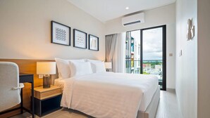 A hotel room with a bed, bedside table, lamp, chair, and a large window offering a view of the city.