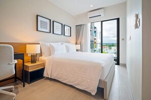 Ein Hotelzimmer mit Bett, Nachttisch, Lampe, Sessel und einem großen Fenster mit Blick auf die Stadt.