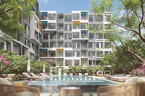 A modern apartment building with a swimming pool, lounge chairs, and lush greenery.