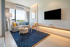 A modern living room with a sofa, armchair, round coffee table, and a large TV mounted on the wall.