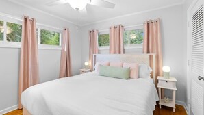 A bedroom with a bed, two bedside tables with lamps, a ceiling fan, and windows with curtains. - 3BR Pool Home | Free Parking | Near Airport + DT (North Charleston)