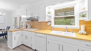 A modern kitchen with white cabinetry, a wooden countertop, a stainless steel range hood, a double sink, and a window with a view of greenery outside. - 3BR Pool Home | Free Parking | Near Airport + DT (North Charleston)