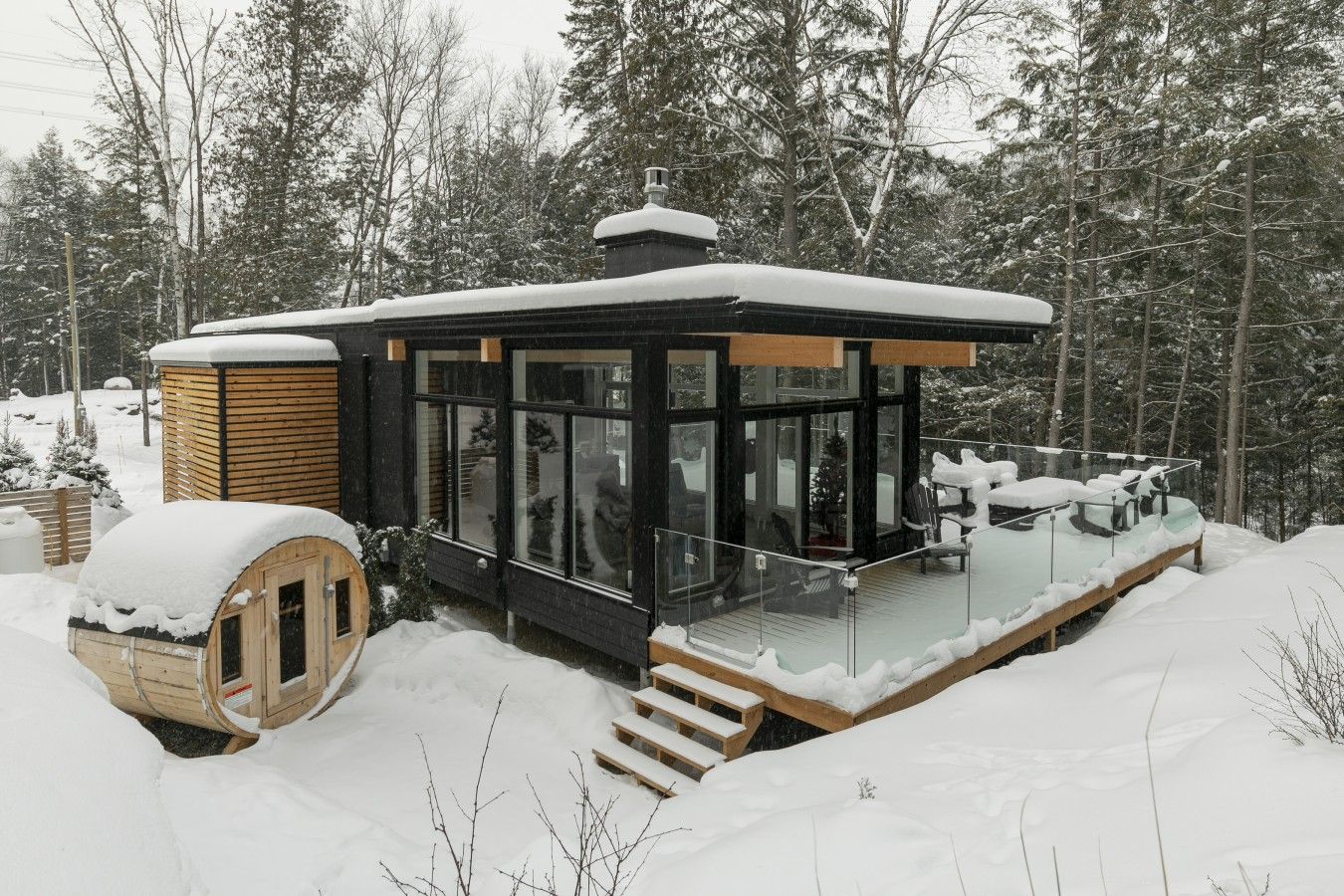A modern cabin with a glass-enclosed porch, wooden deck, and a small cabin-like structure.