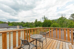 A wooden deck with a table and two chairs, overlooking a green landscape. - DOWNTOWN | FREE shuttle to Ski Resort • Ice Rink (Mont-Tremblant)
