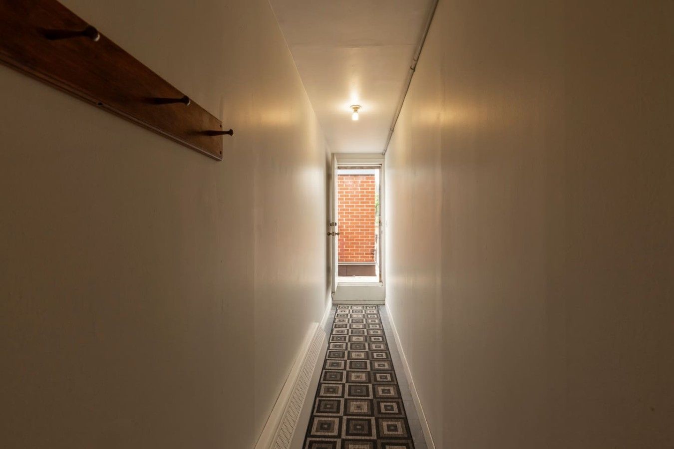 Un couloir étroit, dont le sol est décoré de motifs, mène à une porte dotée d’une fenêtre.