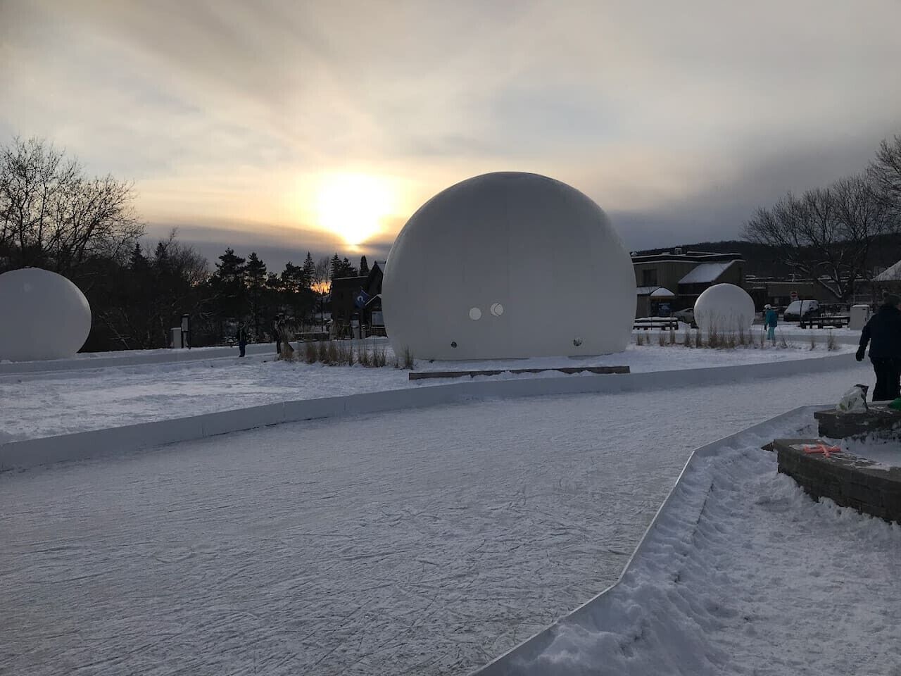 A snow-covered outdoor area with large spherical structures, likely for recreational activities, and a clear sky with the sun setting in the background.