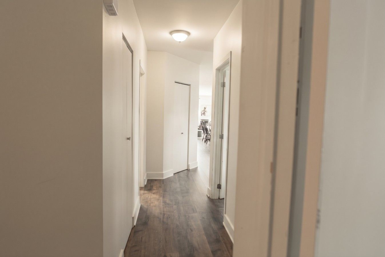A hallway with white walls and wooden flooring leading to a room with a door.