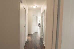 A hallway with white walls and wooden flooring leading to a room with a door. - DOWNTOWN | FREE shuttle to Ski Resort • Ice Rink (Mont-Tremblant)