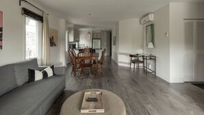 A modern living room with a grey sofa, wooden dining table, and chairs. There is a remote control on a round ottoman. - Downtown | FREE shuttle to Ski Resort • Ice Rink (Mont-Tremblant)