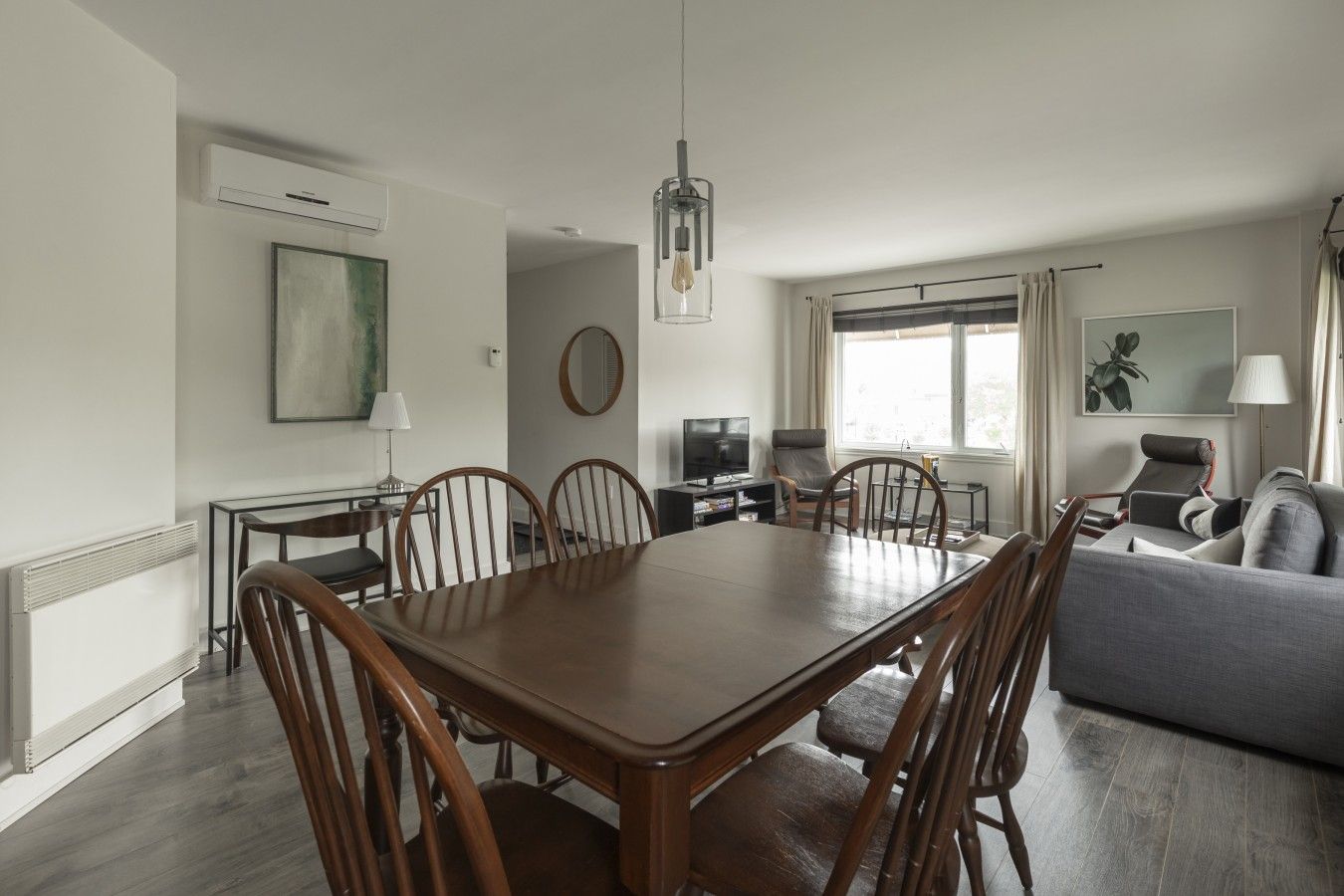 A modern living room with a dining area, a sofa, a TV, and a large window with curtains.