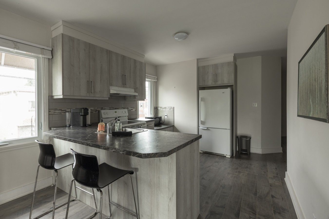 A modern kitchen with a central island, bar stools, and a refrigerator.