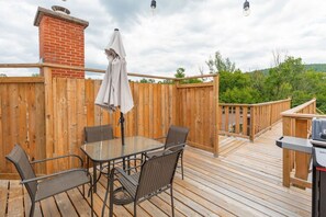 A wooden deck with a glass table and chairs, a barbecue grill, and a wooden fence. - DOWNTOWN | FREE shuttle to Ski Resort • Ice Rink (Mont-Tremblant)