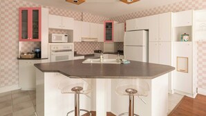 Une cuisine moderne avec un îlot central, des meubles blancs, des touches de rose et un dosseret à carreaux.