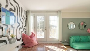 Une pièce spacieuse avec une grande fenêtre, un canapé vert et un pouf rose.