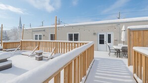 Une terrasse extérieure recouverte de neige, dotée de rampes en bois et de chaises longues.