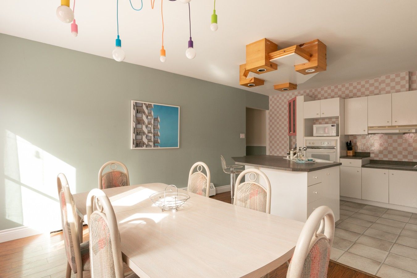 A modern kitchen with white cabinets, a central island, and a dining area with a light-colored table and wicker chairs.