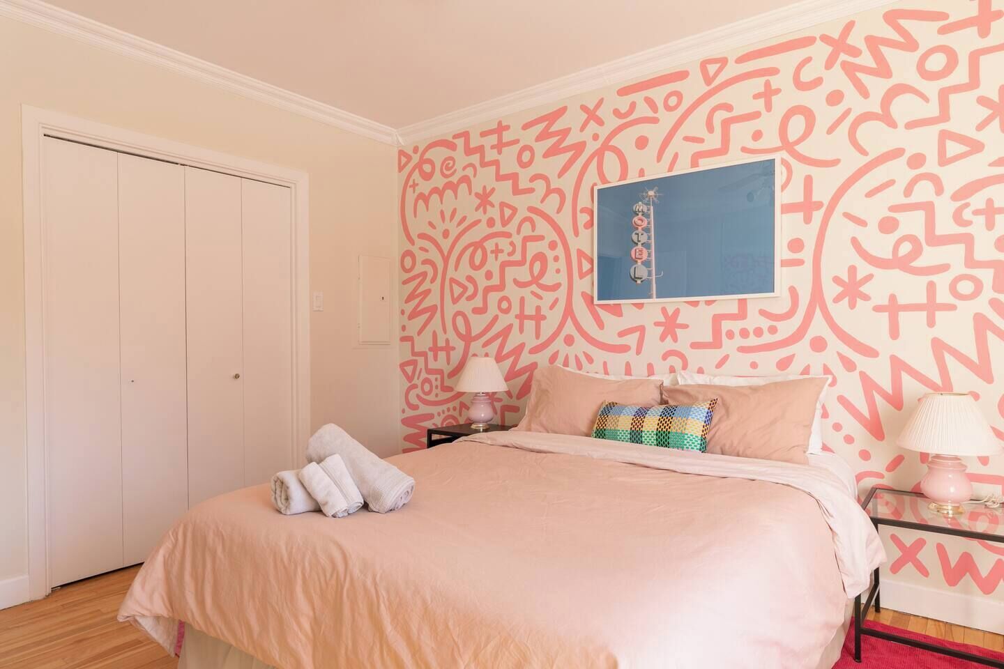 A bedroom with a bed, pillows, a nightstand, a lamp, and a wall with a geometric pattern.