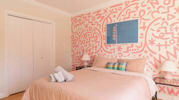 A bedroom with a bed, pillows, a nightstand, a lamp, and a wall with a geometric pattern.