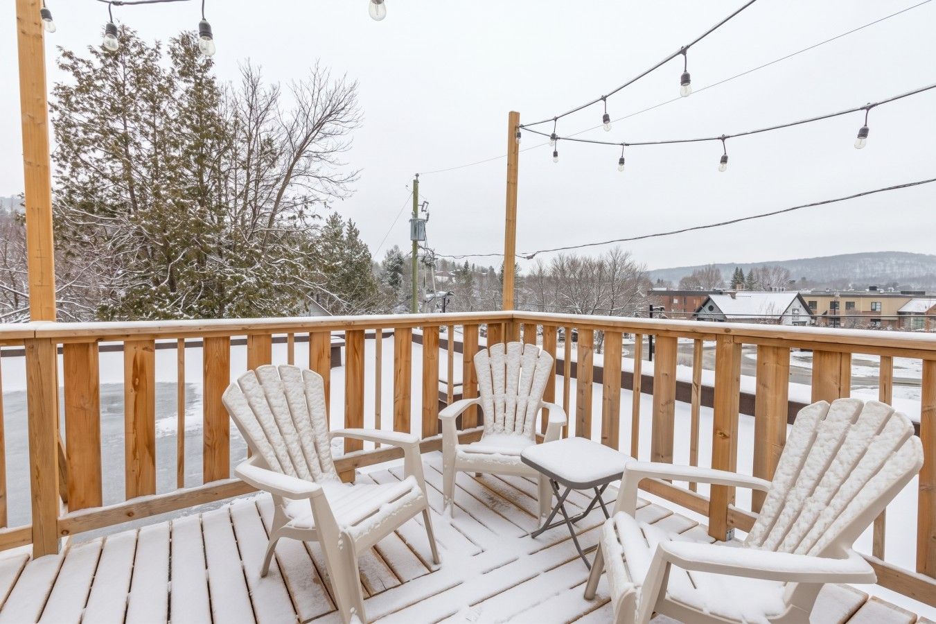 Une terrasse enneigée, dotée de rampes en bois et de deux fauteuils Adirondack.
