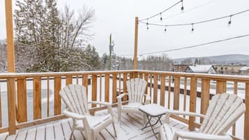 Une terrasse enneigée, dotée de rampes en bois et de deux fauteuils Adirondack.