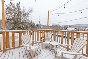 Une terrasse enneigée, dotée de rampes en bois et de deux fauteuils Adirondack.