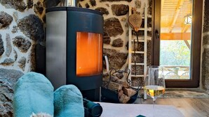 Ein gemütliches Zimmer mit Steinwand, Kaminofen, einem Glas Wein und einem Buch auf dem Tisch.