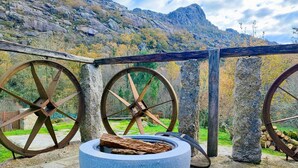 Ein Steinkamin mit einem Holzscheit, umgeben von großen Holzwagenrädern, vor einer Berglandschaft.