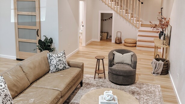 Un salón espacioso con techo alto, una escalera de madera, un sofá, una mesa redonda y vista al piso superior.
