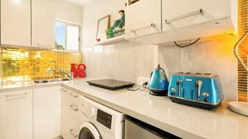 A modern kitchen with white cabinets, a washing machine, a kettle, and a blue toaster.