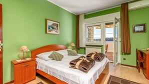 Une chambre d’hôtel comprenant un lit, une table de chevet, un bureau, une chaise, une fenêtre avec vue et une porte donnant sur un balcon.