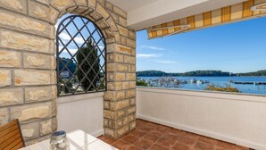 Un balcon aux murs en pierre, une vue sur un port de plaisance et une table sur laquelle se trouve un bocal rempli de petits cailloux.