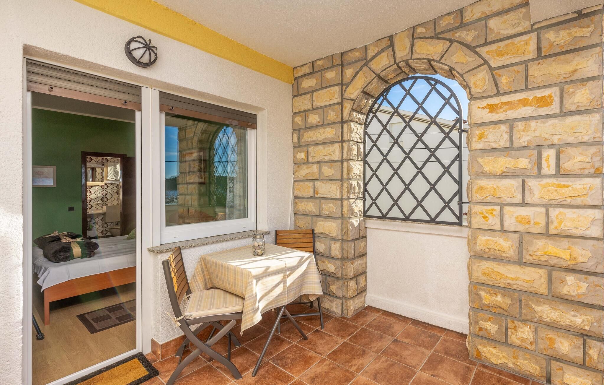 Un petit balcon avec une table et une chaise, un mur en pierre et une fenêtre ornée d’une grille métallique.