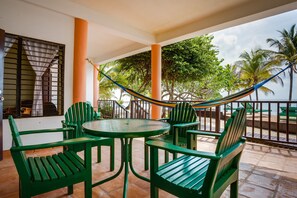 Relax in a serene outdoor space with a round table, four chairs, and a hammock suspended between pillars, offering a tranquil view of the surrounding water and lush palm trees.