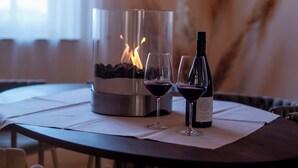 Una mesa redonda con una chimenea de vidrio, dos copas de vino y una botella de vino.