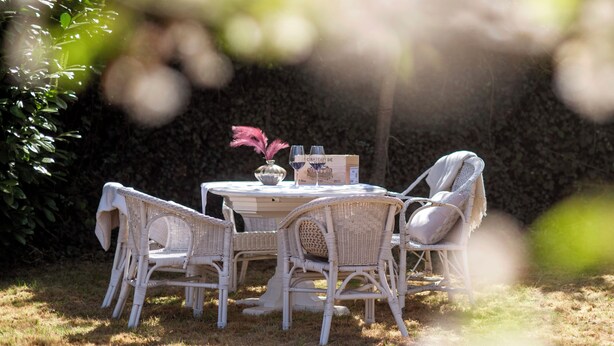 Un conjunto de mesa y sillas de mimbre, un florero y una copa de vino en un espacio al aire libre.