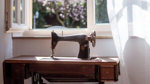 Una máquina de coser Singer antigua sobre una mesa de madera junto a una ventana con cortinas blancas.