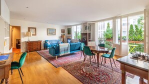 A spacious living room with a blue sofa, a dining table with chairs, and a large window offering a view of the outdoors. - Paris Chic Trocadero Private apartment in Passy 500 meters from the Eiffel Tower  (Paris)