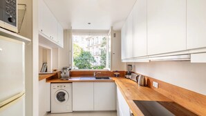 A compact kitchen with a washing machine, a sink, and a window with a view of buildings. - Paris Chic Trocadero Private apartment in Passy 500 meters from the Eiffel Tower  (Paris)