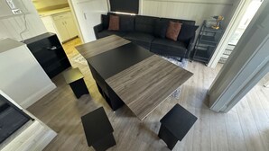 Un salon moderne avec une table à manger en bois foncé, des canapés noirs et une petite table d’appoint sur laquelle se trouve une perceuse.