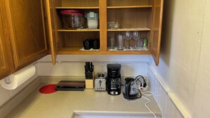 Une cuisine avec des meubles de rangement en bois, un plan de travail sur lequel se trouvent un grille-pain, une machine à café et une boîte de thé.