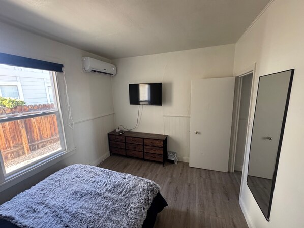 Une chambre à coucher avec un lit, une commode, un téléviseur fixé au mur et une fenêtre donnant sur une clôture en bois.