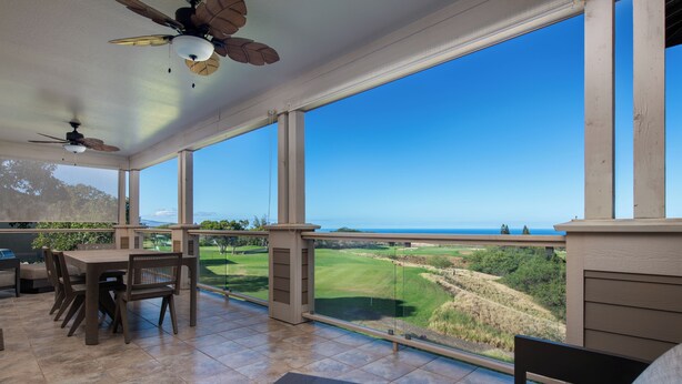 A covered patio with a dining table and chairs, large windows offering a view of a golf course and distant landscape.