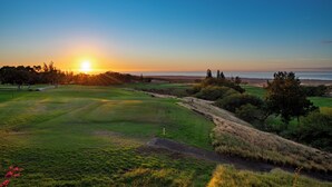 A golf course with a sunset view, a flagstick, and a distant body of water.