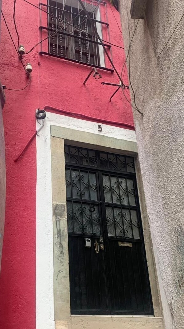 A narrow alleyway with a red building on one side and a white building on the other. A black gate with a number '5' above it is visible. - Garambullo Inn (Guanajuato)