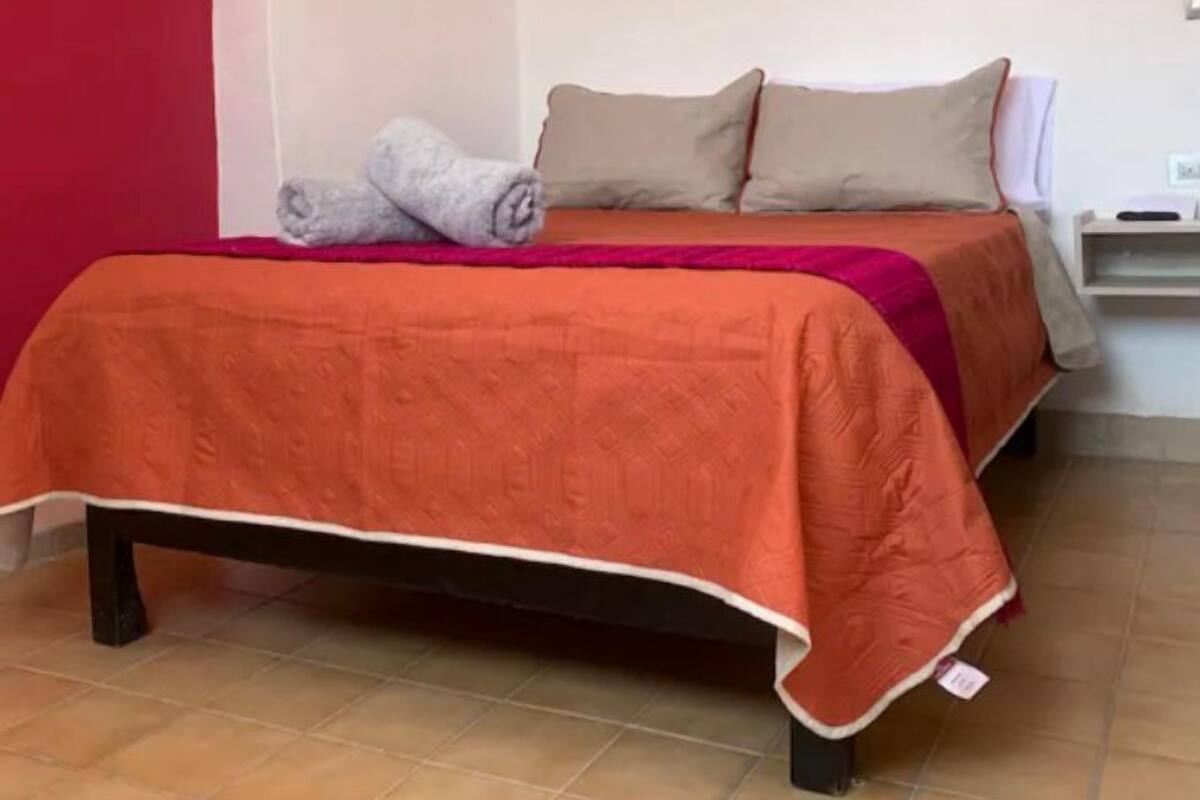 Un lit avec une couvre-lit rouge et orange, une couverture grise et deux oreillers.