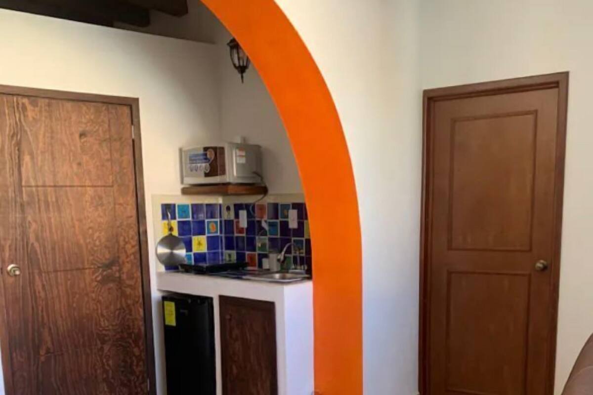 Un espace de vie compact comprenant un coin cuisine, une porte en bois et un sol carrelé.
