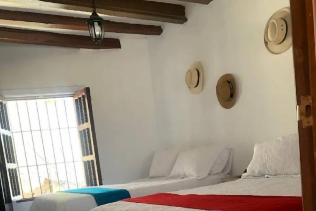 Une chambre d’hôtel avec deux lits, une fenêtre avec des barreaux et un ventilateur au plafond.