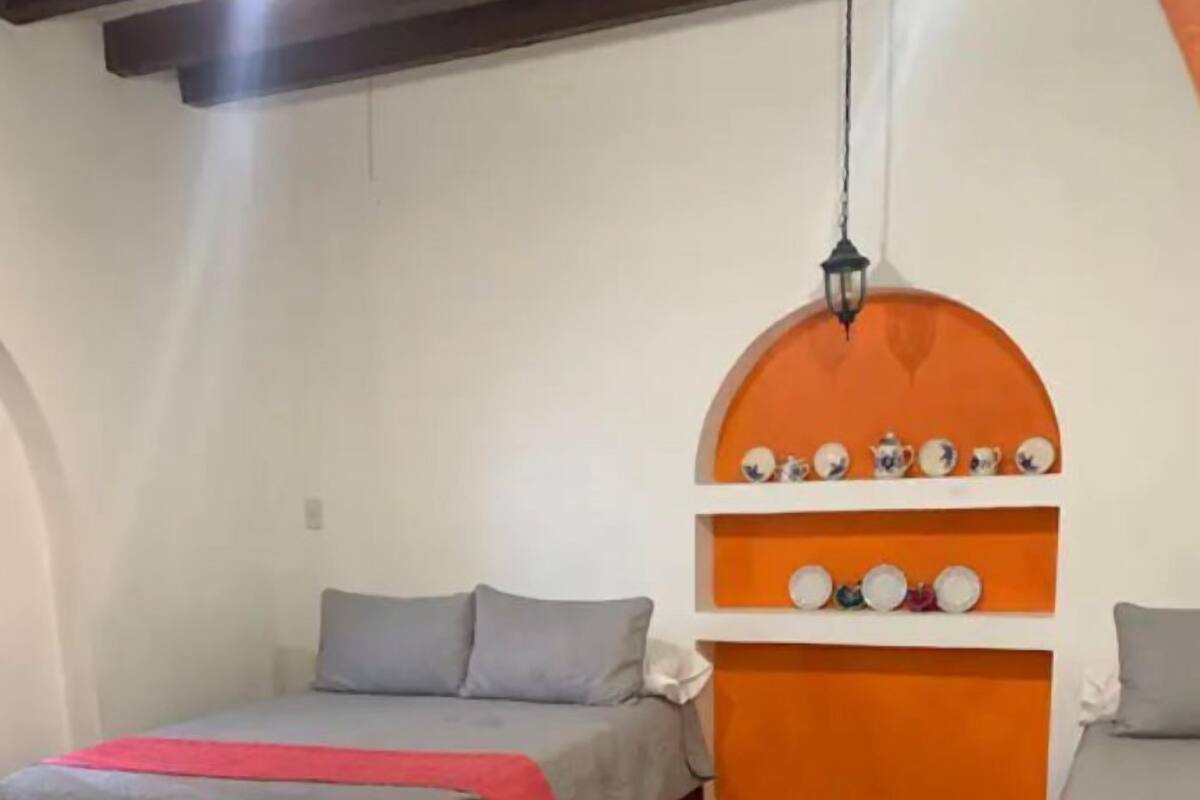 Une chambre avec deux lits, un sol carrelé et une étagère ornée d’objets décoratifs.